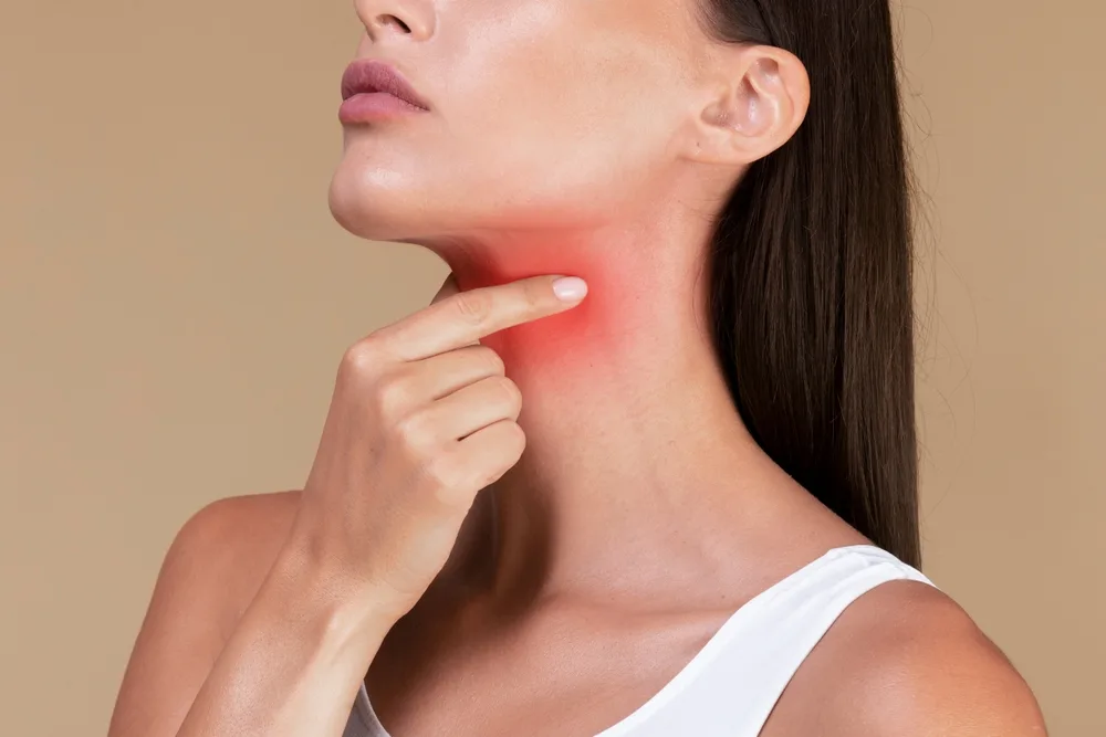 Woman pointing to red highlighted area on her neck indicating thyroid pain or swelling