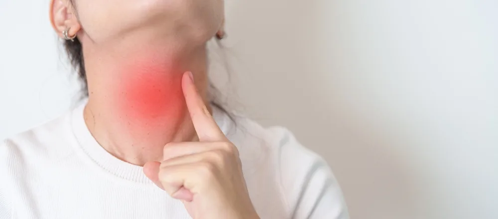 Woman touching her neck with red highlighted area indicating thyroid pain or inflammation