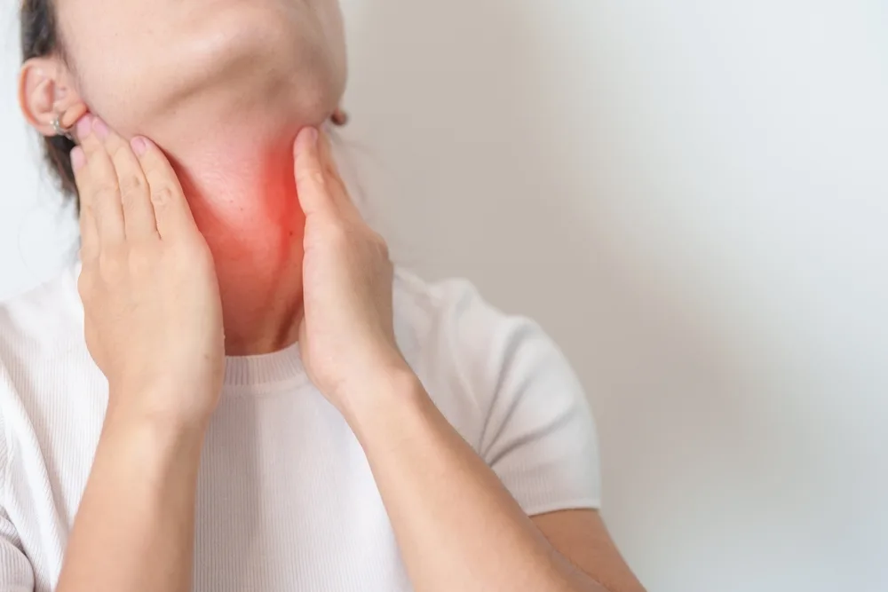 Person holding neck with red highlighted pain area on throat