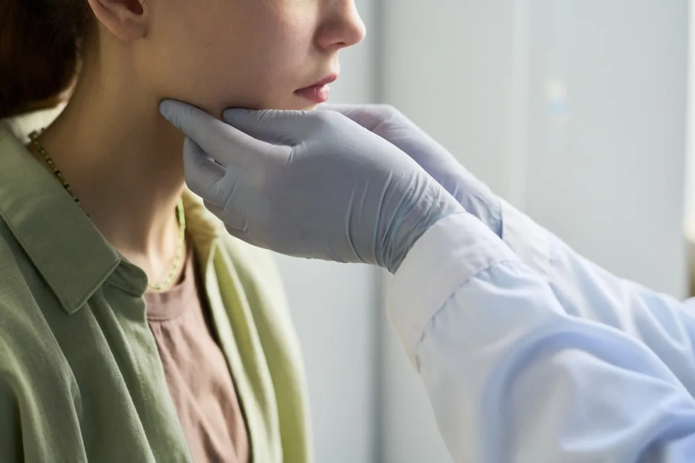 Healthcare provider in blue gloves examining patient's neck and jawline