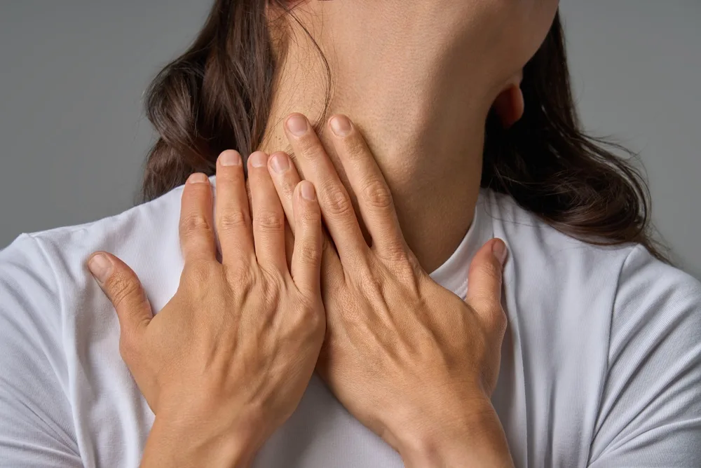 Woman holding her neck with both hands, expressing discomfort