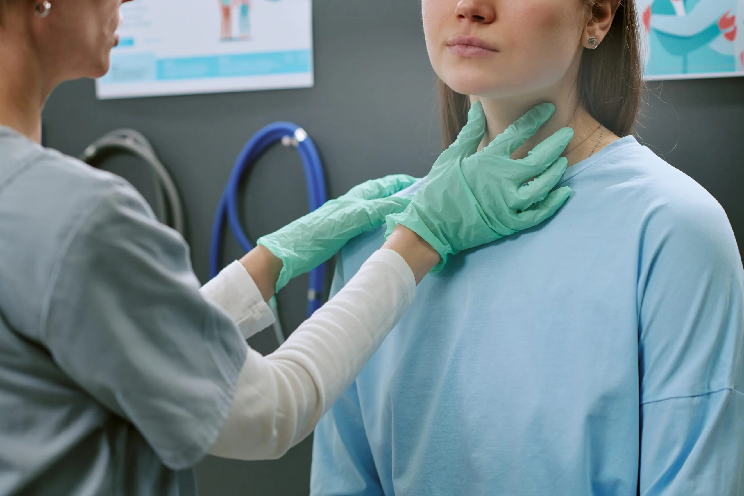 Clinician examining patient's neck with gloved hands in medical office setting