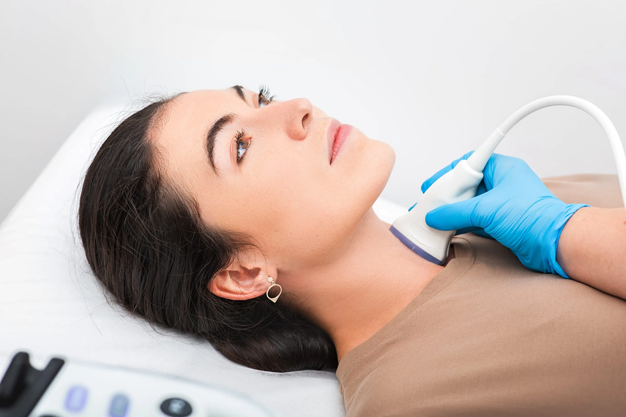 Clinician in blue gloves performing ultrasound examination of patient's neck and thyroid area