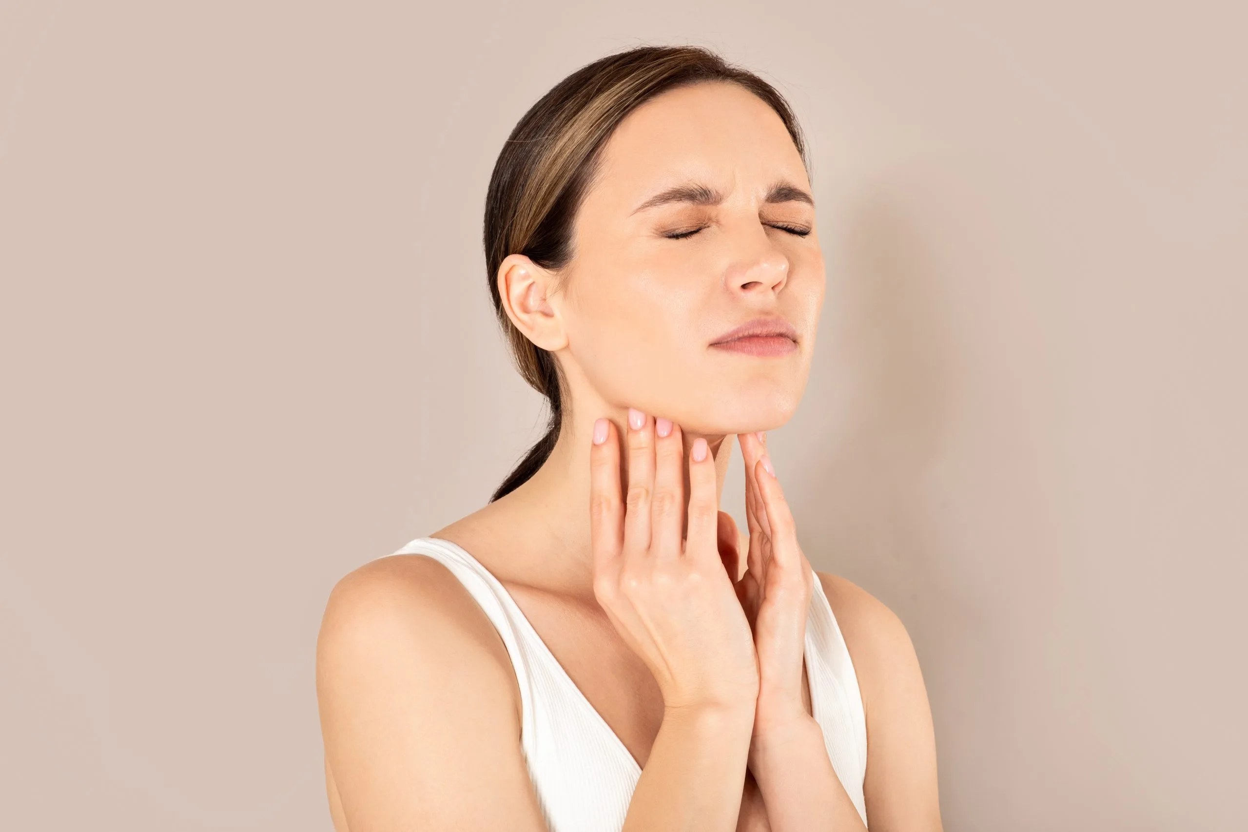 Woman holding her neck and throat in discomfort, illustrating pharyngitis or tonsillitis symptoms