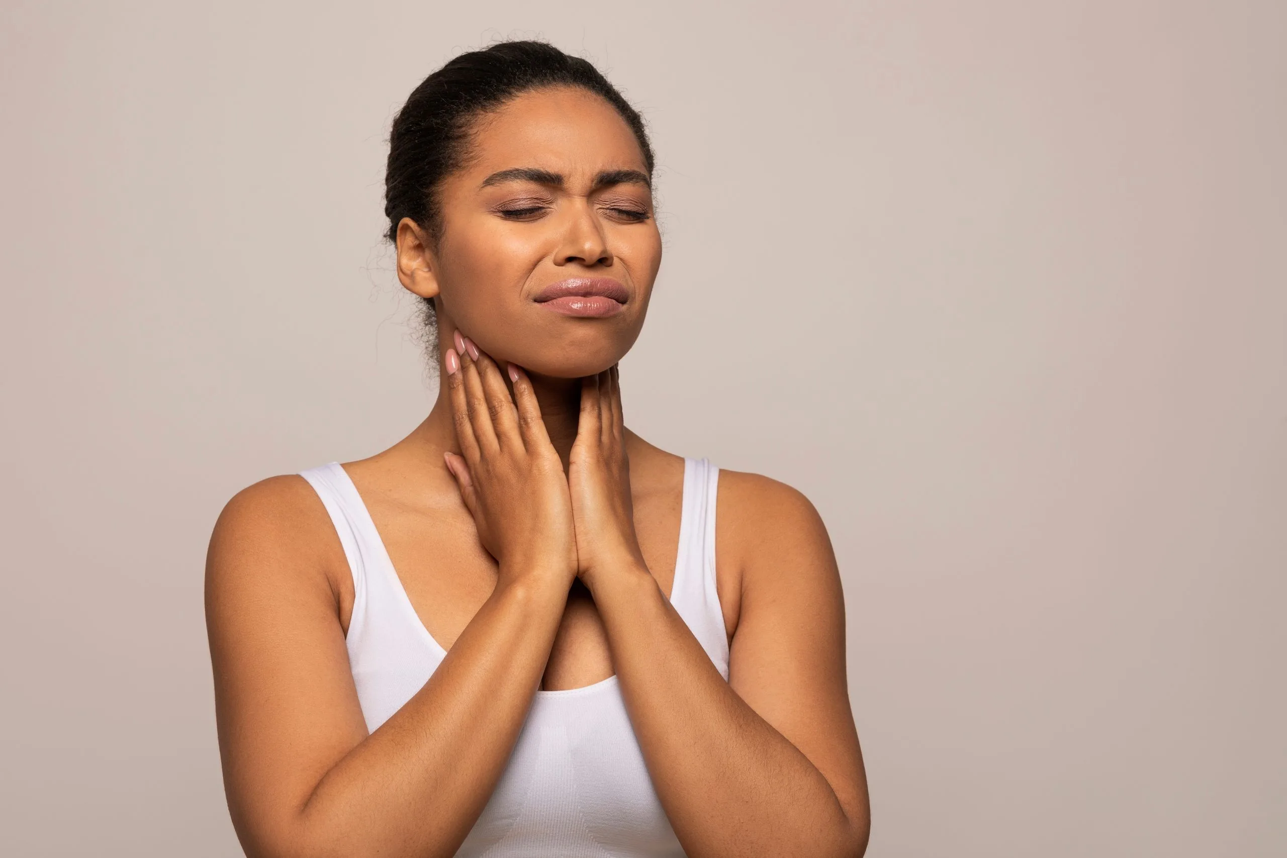 Woman touching her neck and throat in discomfort, expressing sore throat or throat pain