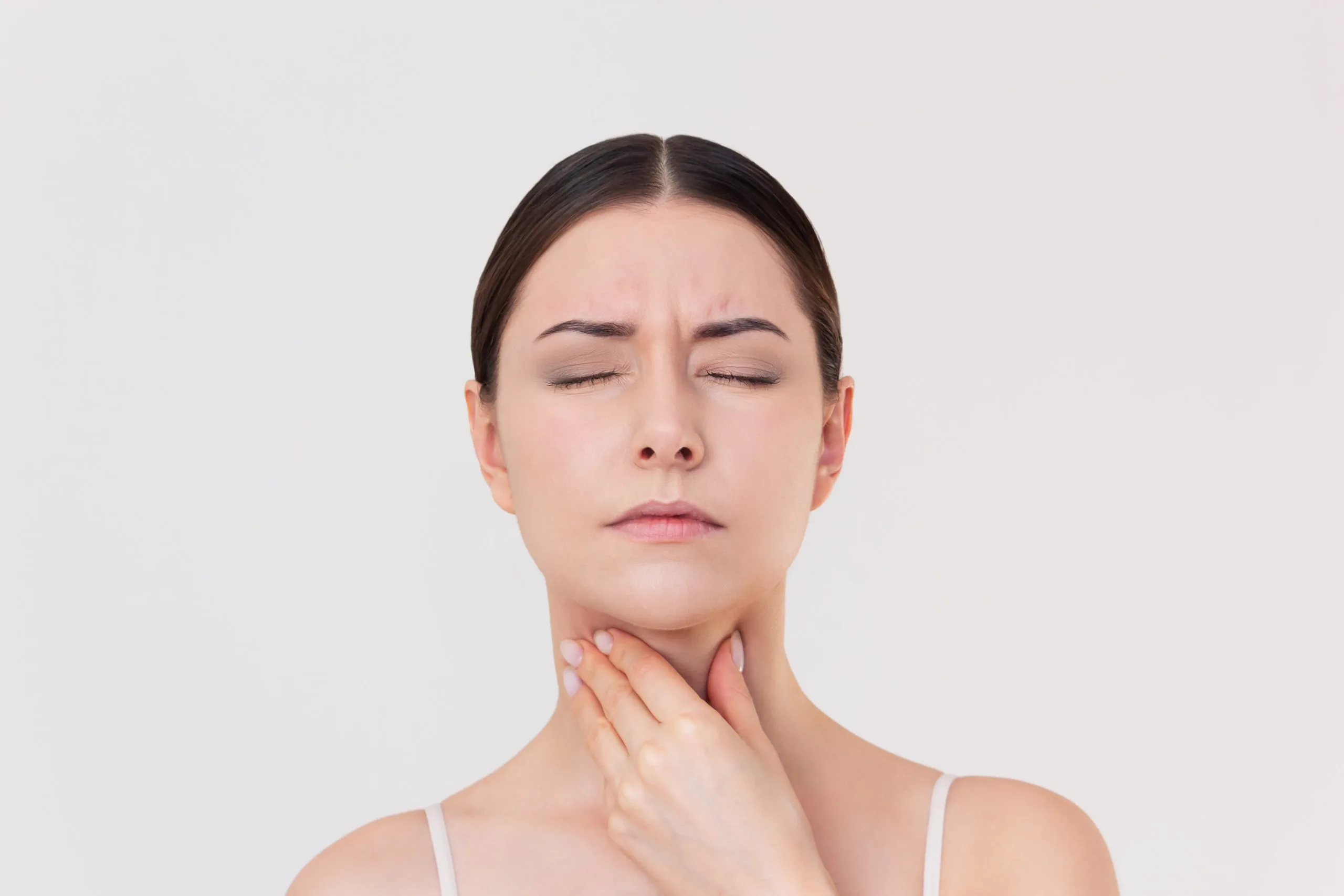 Woman touching her neck with a pained expression, indicating throat discomfort