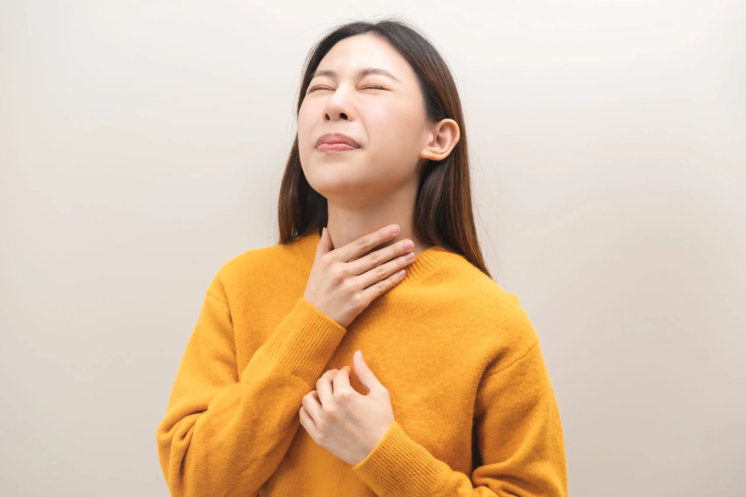 Woman in yellow sweater holding her throat, experiencing neck discomfort