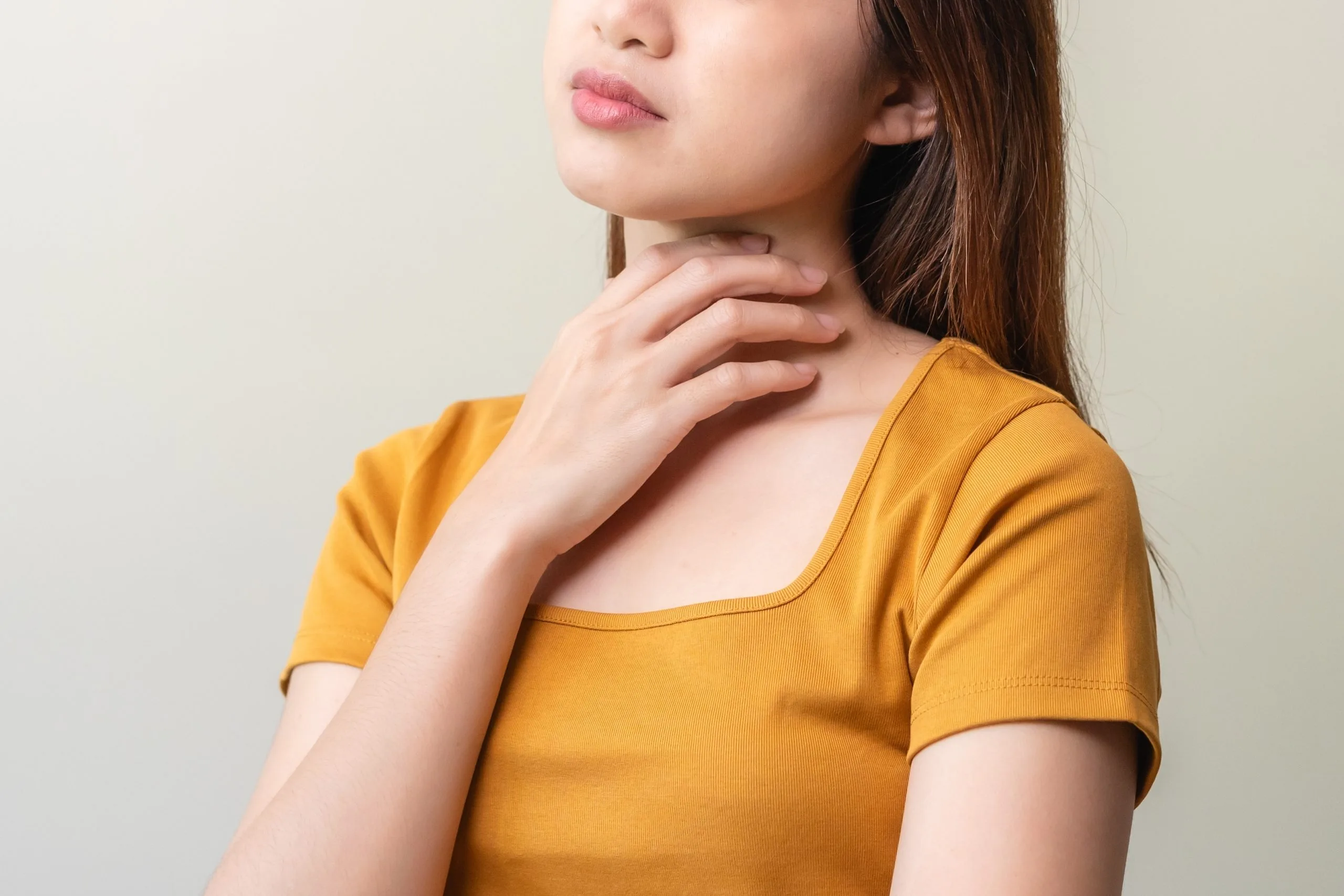 Woman touching her neck and throat area, experiencing soreness or discomfort