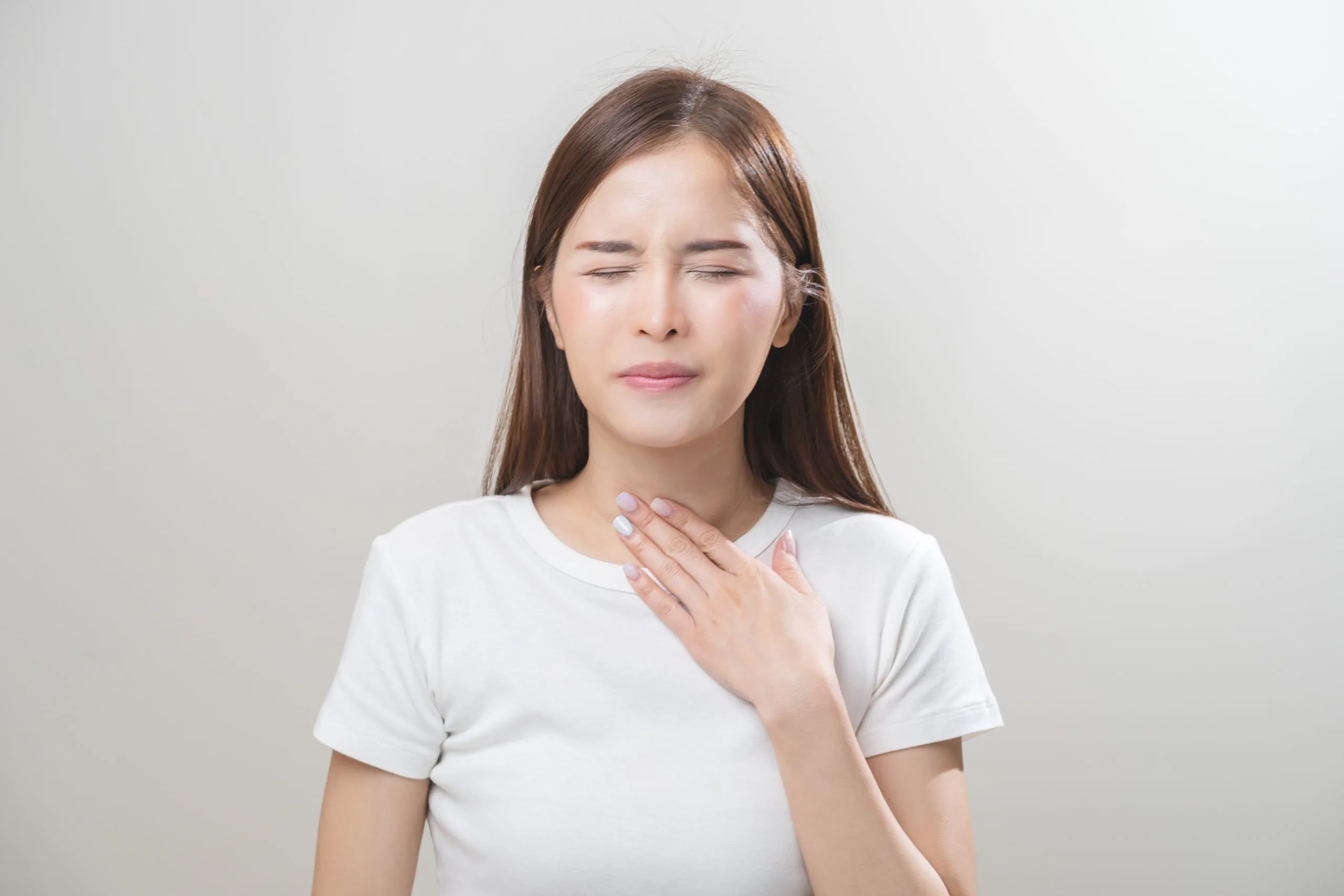 Woman touching her neck with a pained expression, suggesting thyroid discomfort
