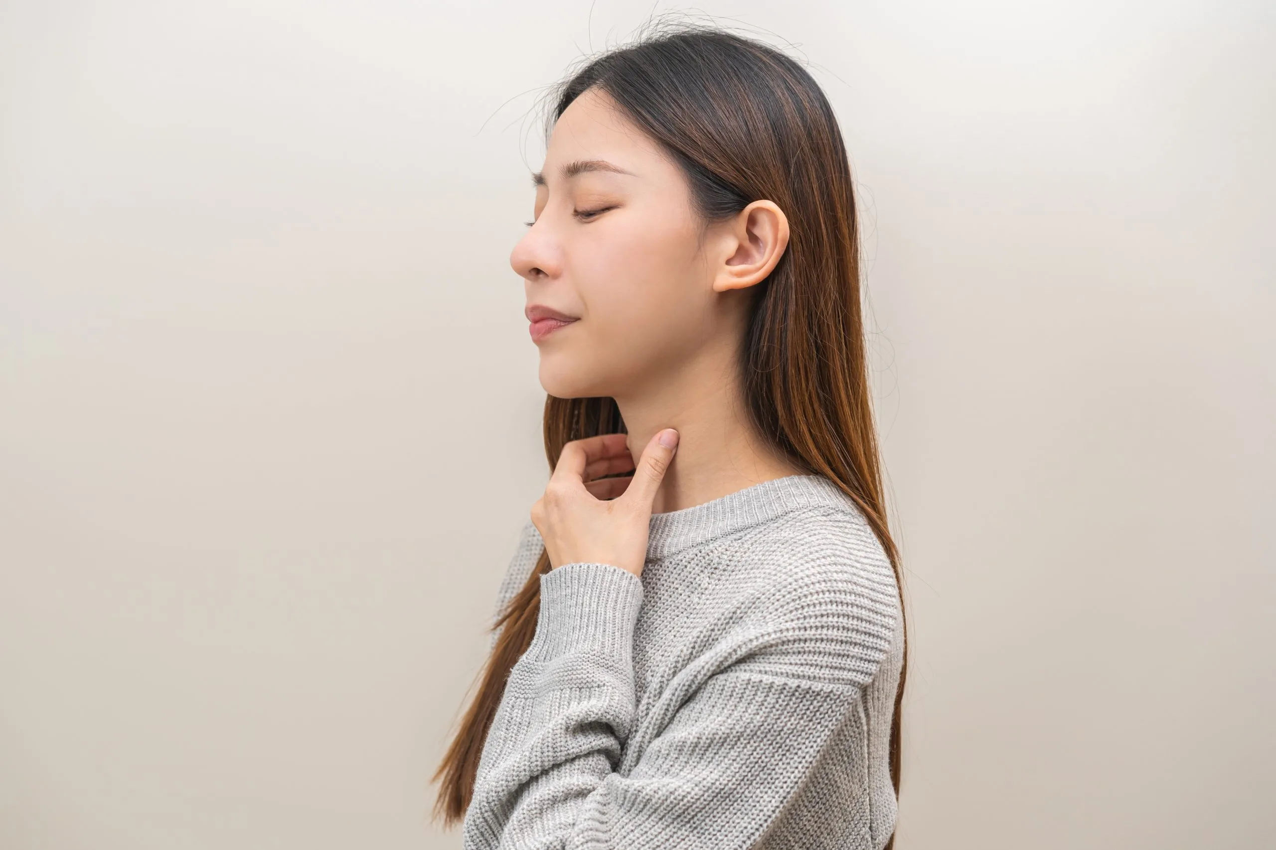 Woman touching her neck and throat area against a neutral background