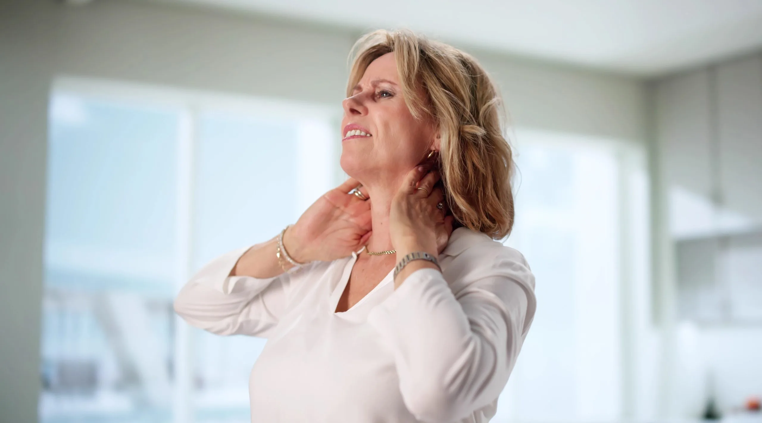Senior woman holding her neck and grimacing from thyroid pain