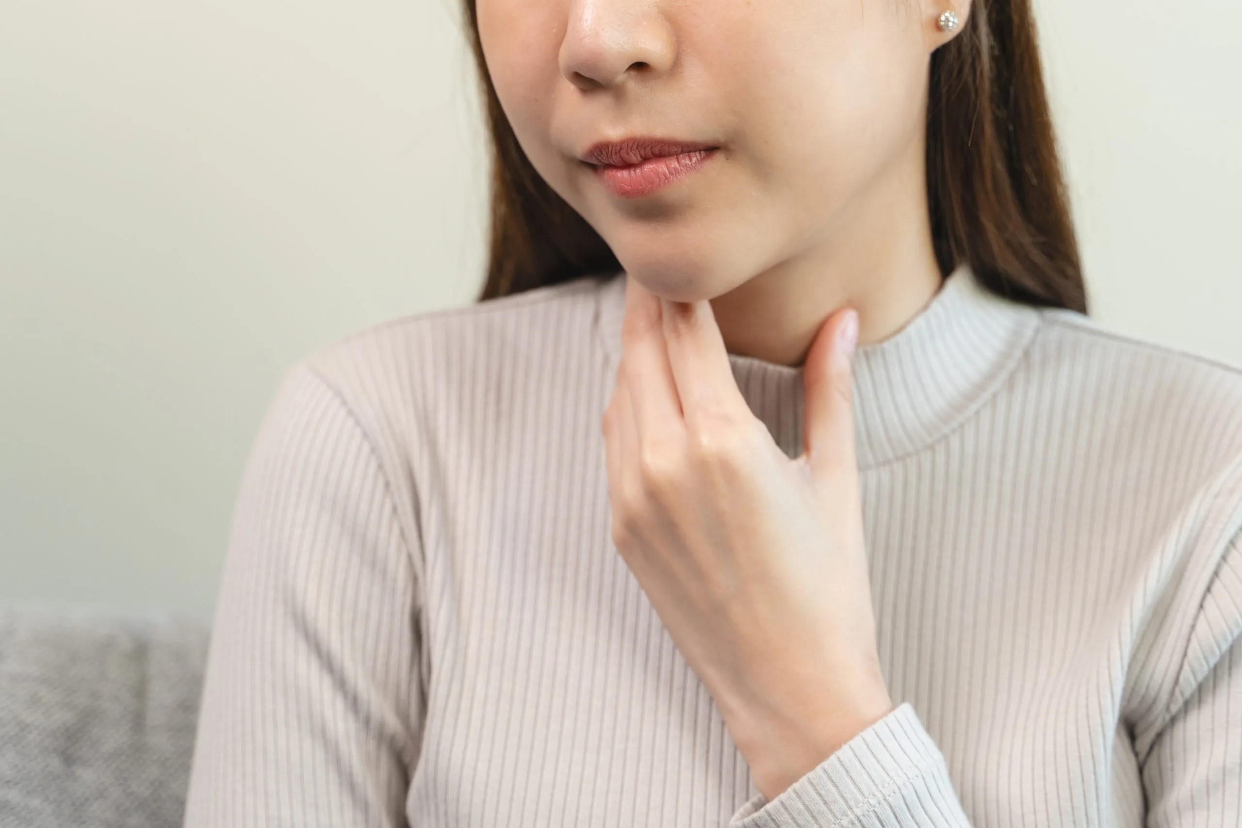 Woman touching her neck and throat area, illustrating thyroid-related symptoms