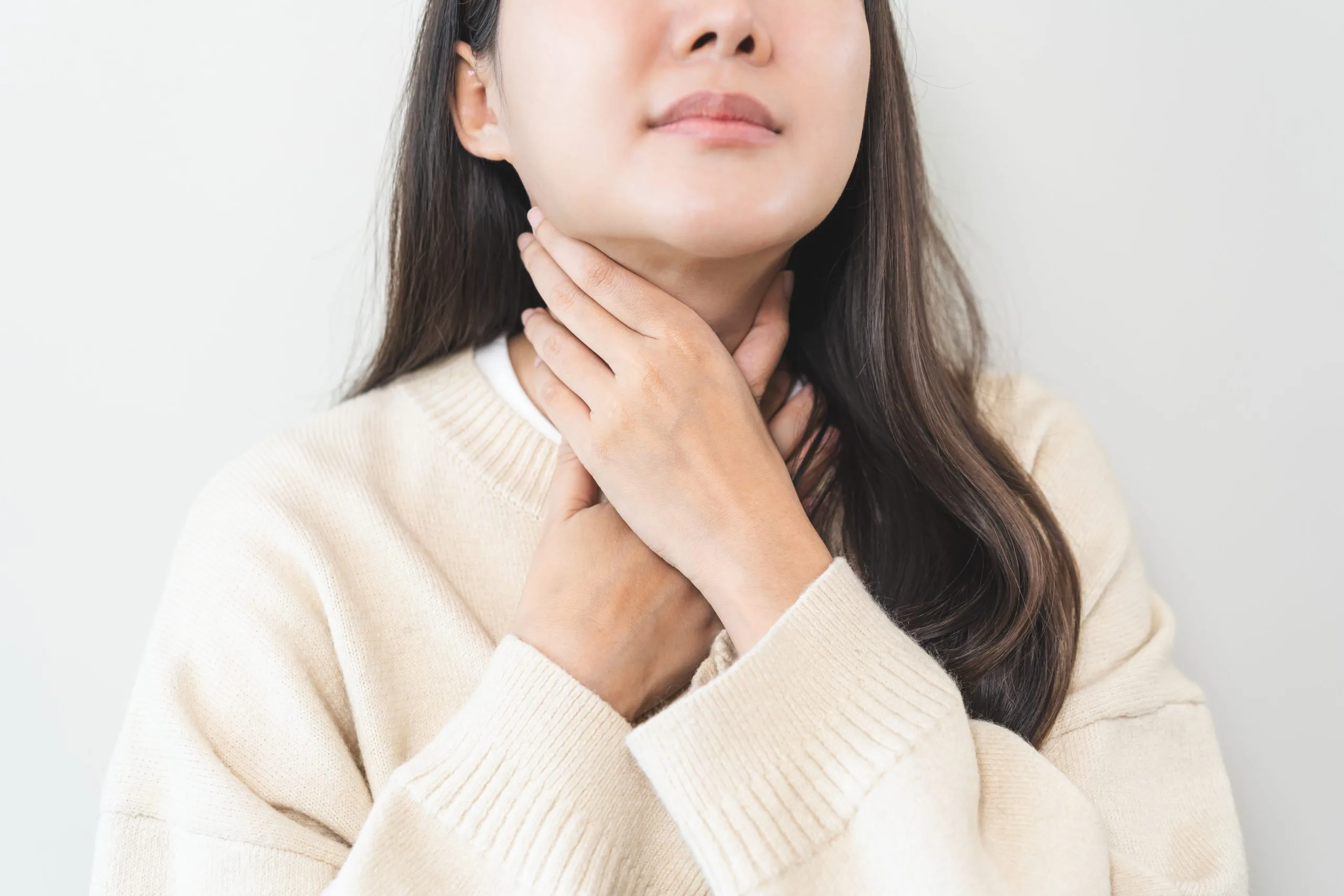 Woman touching her neck with both hands, suggesting thyroid discomfort or swelling