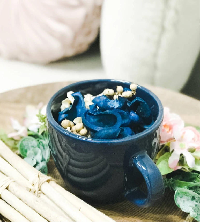 Blue mug with blue rose designs and gold accents surrounded by fresh flowers