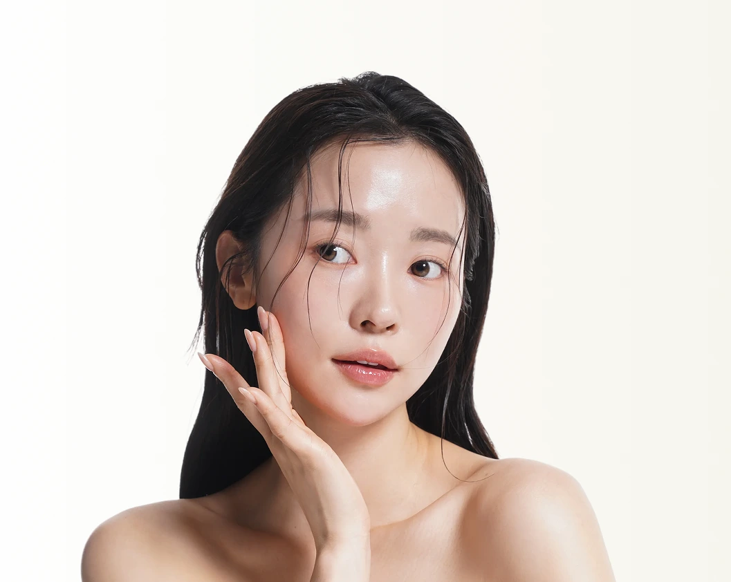Woman with clear, radiant skin touching her face against a neutral background