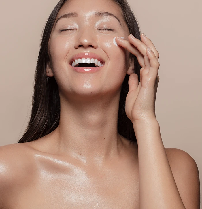 Woman smiling with eyes closed, touching her glowing skin