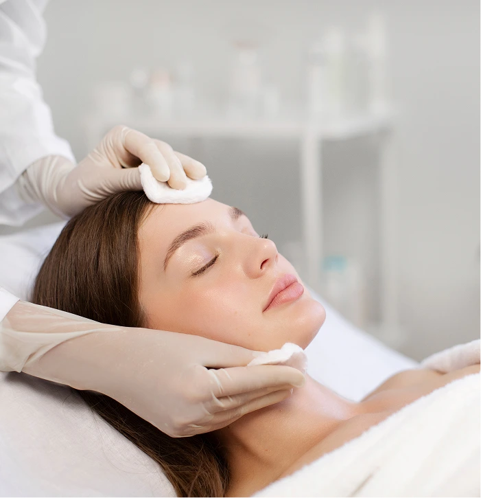Esthetician cleansing woman's forehead with cotton pad during facial treatment