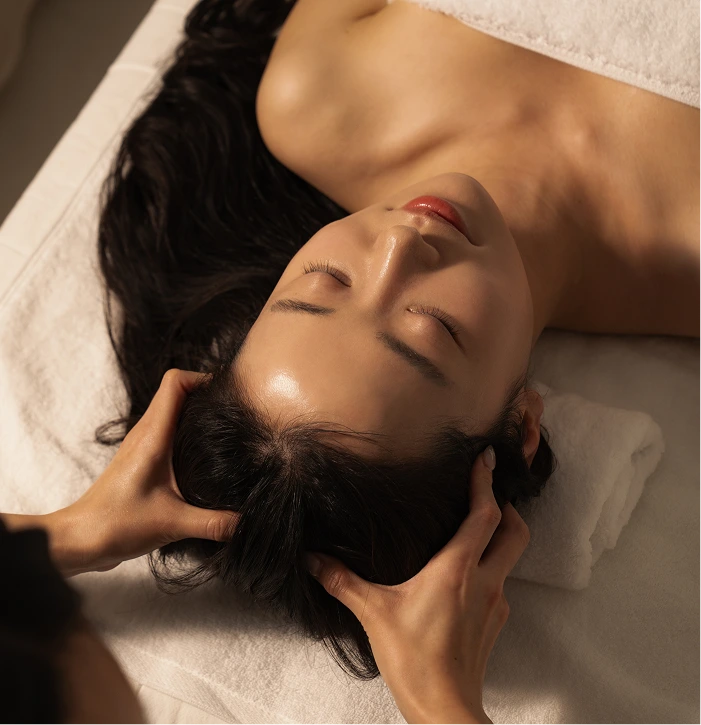Esthetician performing scalp massage on relaxed patient during Korean scalp massage treatment