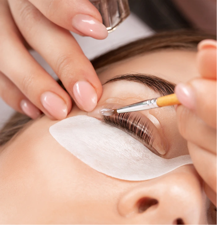 Technician applying lash lift treatment to client's eye with brush on white pad