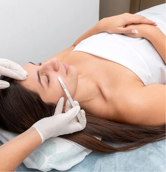 Esthetician performing dermaplaning on client's face with specialized tool