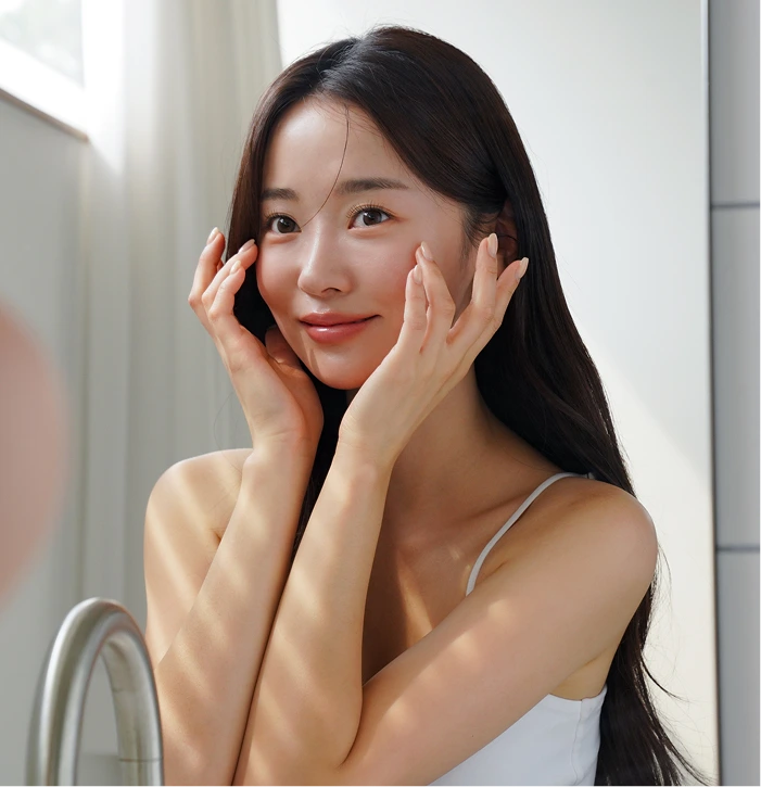 Woman touching her face with both hands near a mirror, smiling with radiant complexion