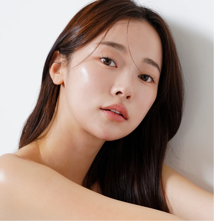 Woman with long dark hair and glowing skin, looking directly at camera with neutral expression