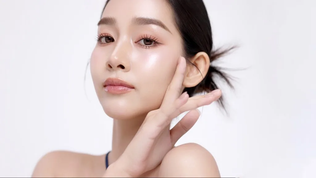 Woman with glowing skin touching her face against a white background
