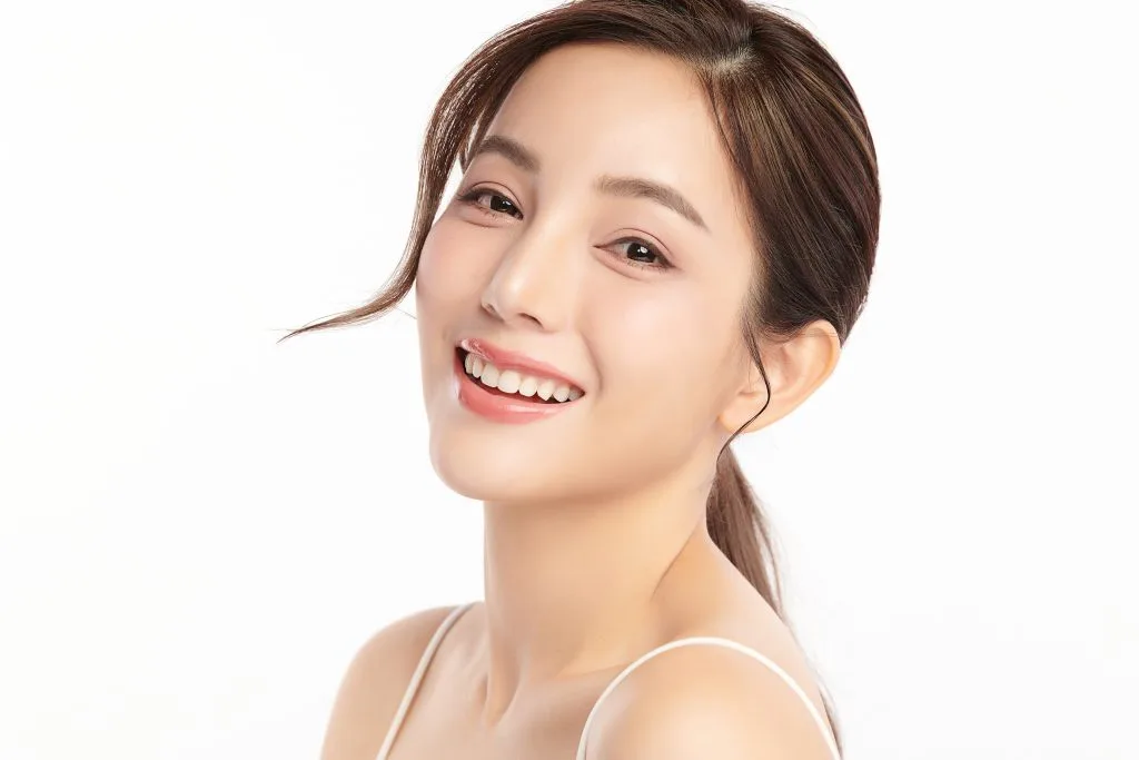 Woman with clear, radiant skin smiling at camera against white background
