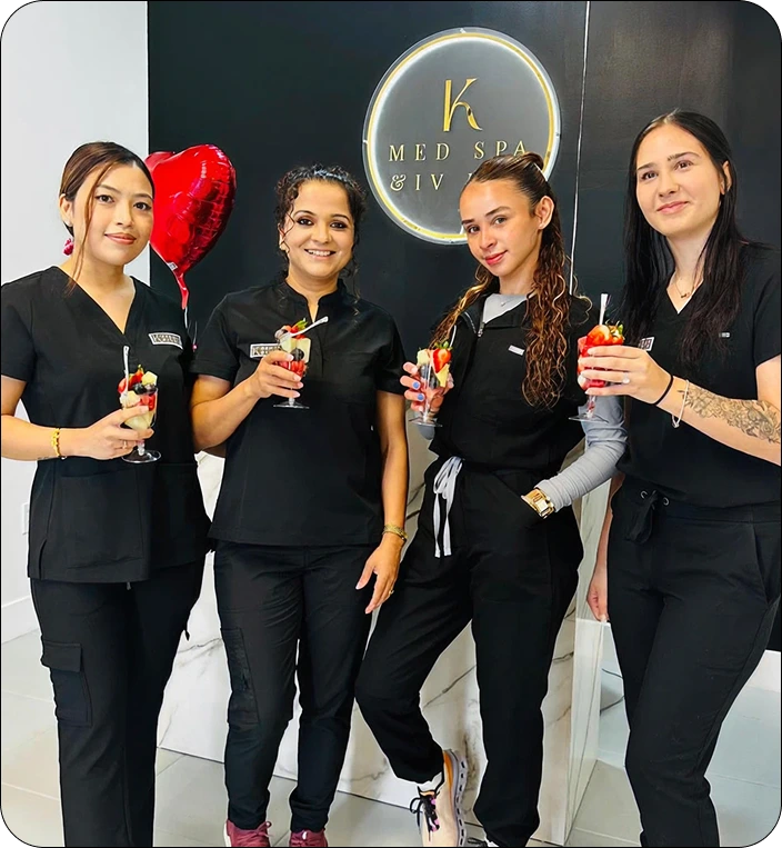 Four K Med Spa & IV staff members in black uniforms holding cocktails in front of illuminated K Med Spa & IV logo