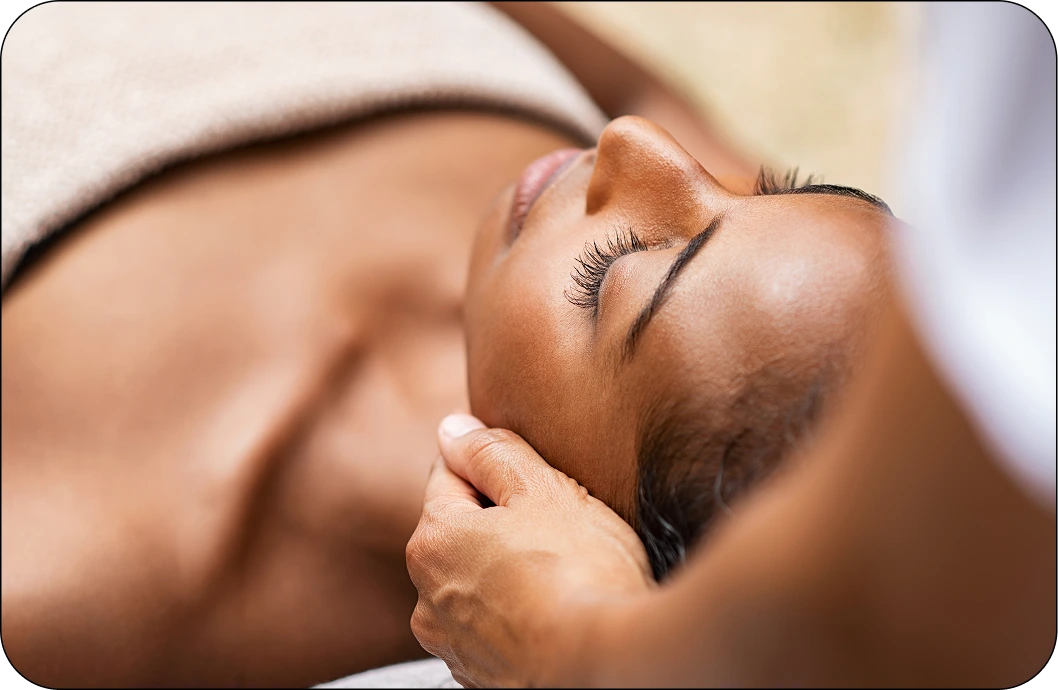Practitioner performing facial massage on relaxed client's cheek and jawline