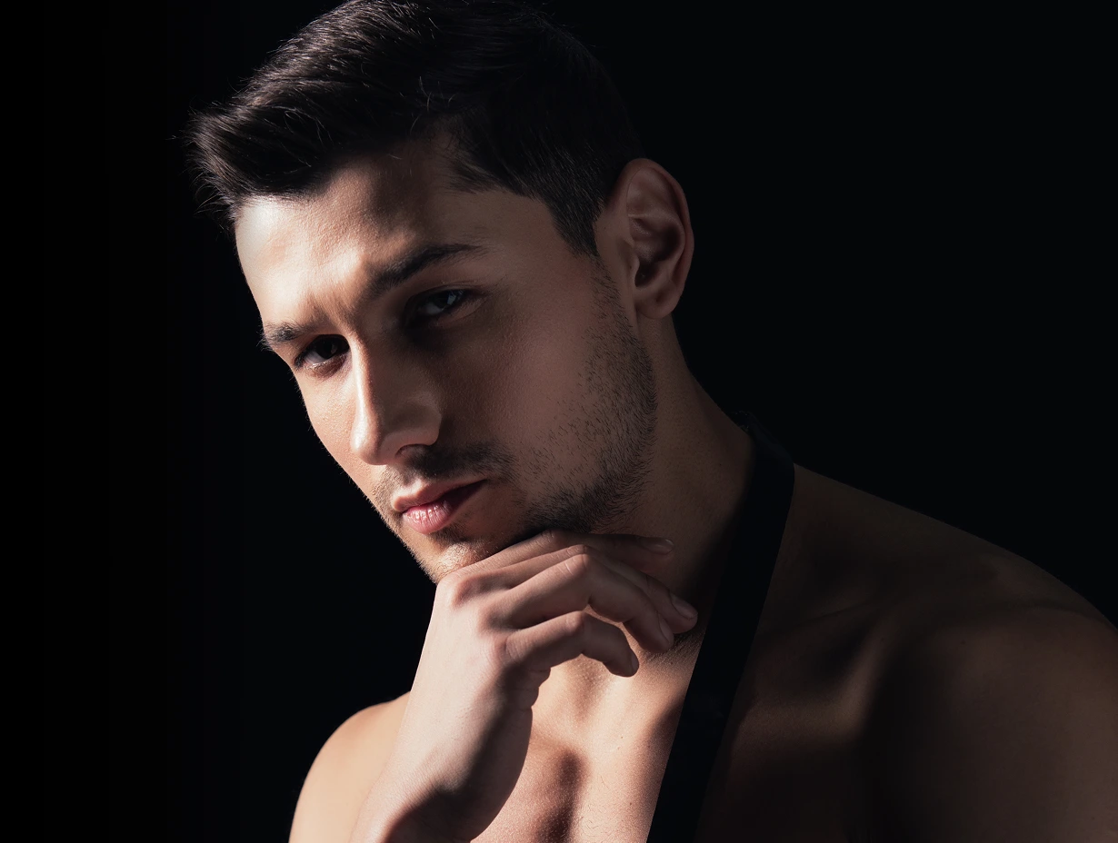 Man with hand to chin looking downward against black background
