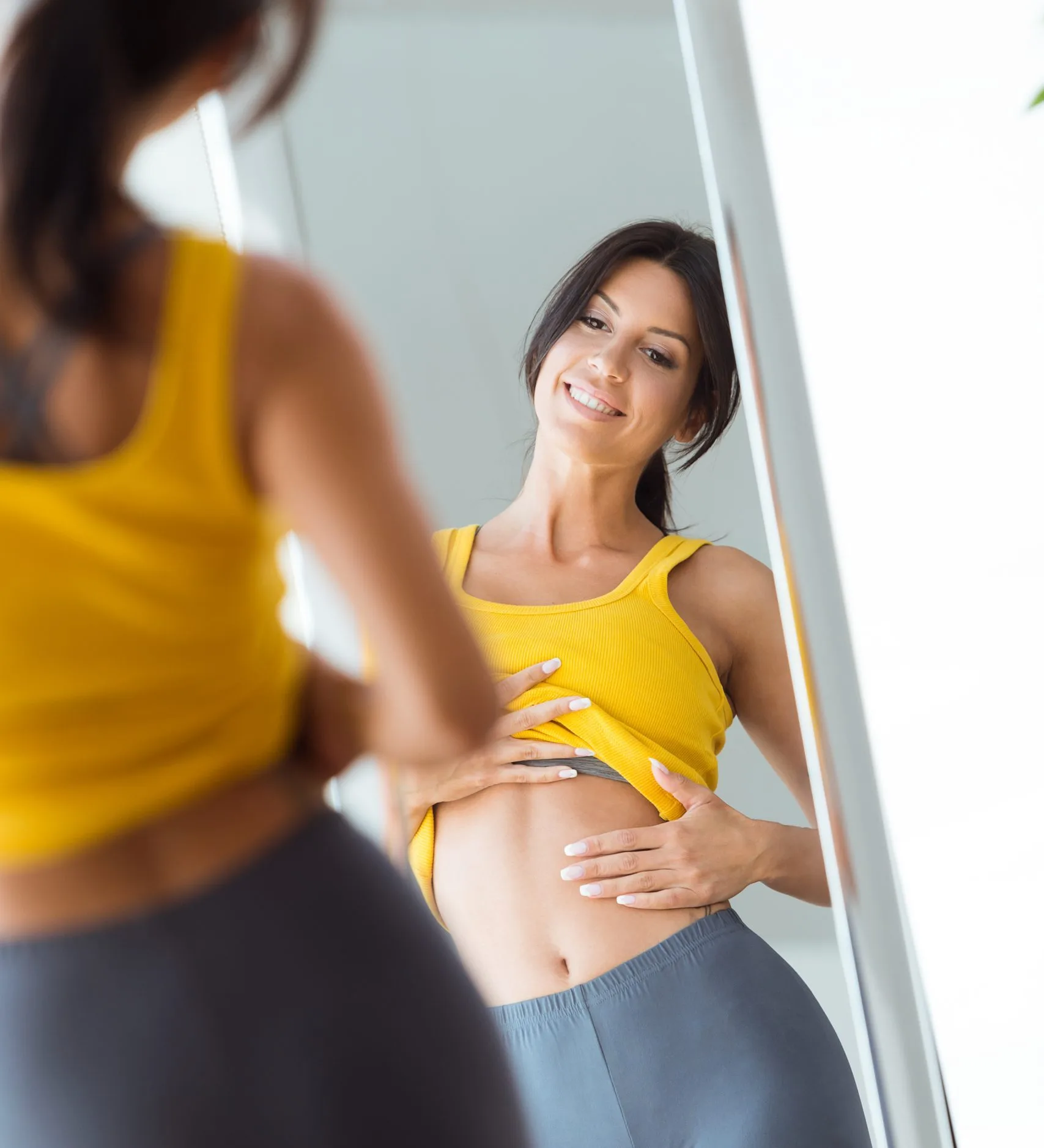 Woman in yellow top smiling while viewing her reflection in a mirror