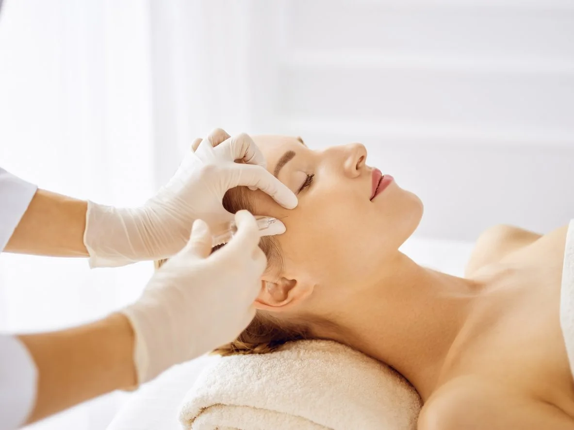 Gloved hands examining a patient's forehead and temple area during a cosmetic consultation