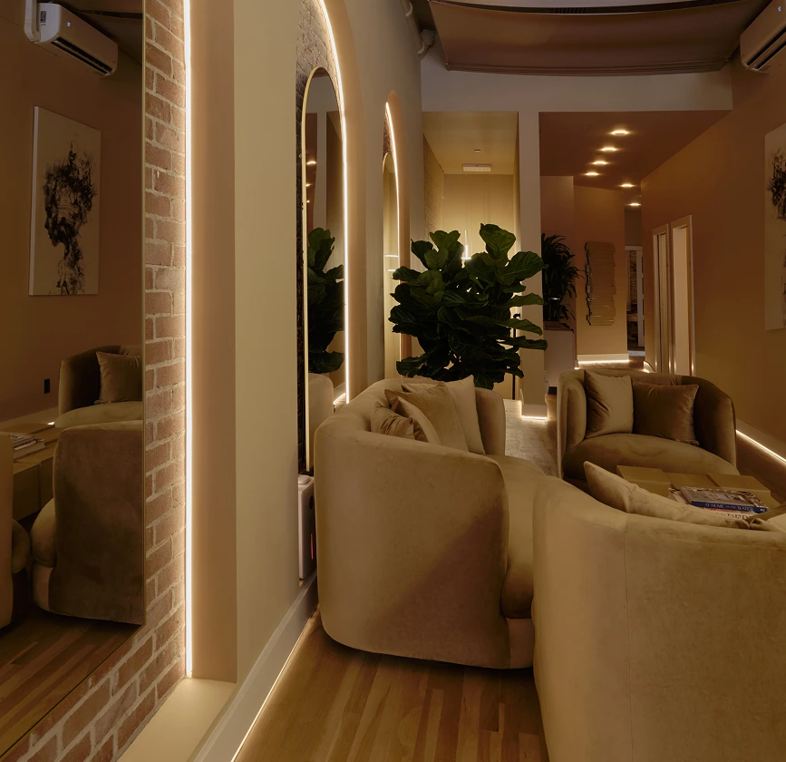 Modern waiting area at La Reservé Aesthetics with cream seating, neon-lit mirrors, and potted plants