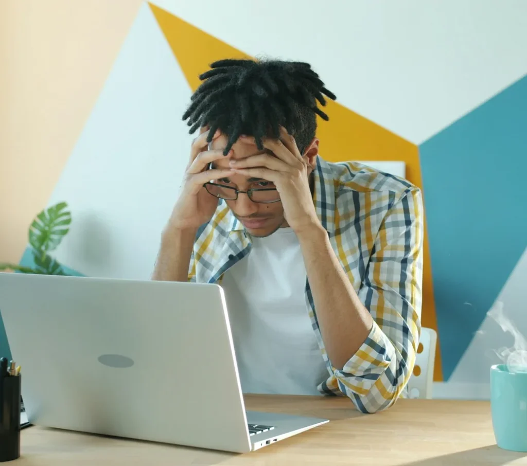 Stressed young man with his head in his hands at a laptop