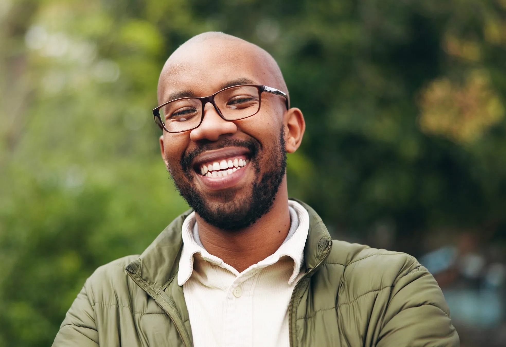 Smiling man in glasses and olive jacket outdoors in a park