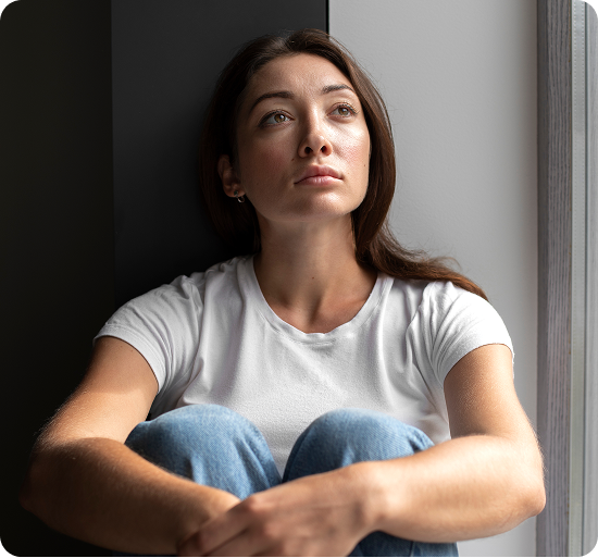 Woman in white t-shirt sitting against wall with contemplative expression