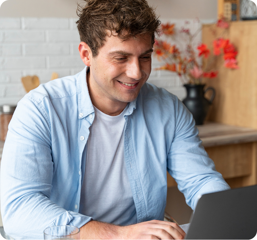 Man in light blue shirt smiling while using laptop at home