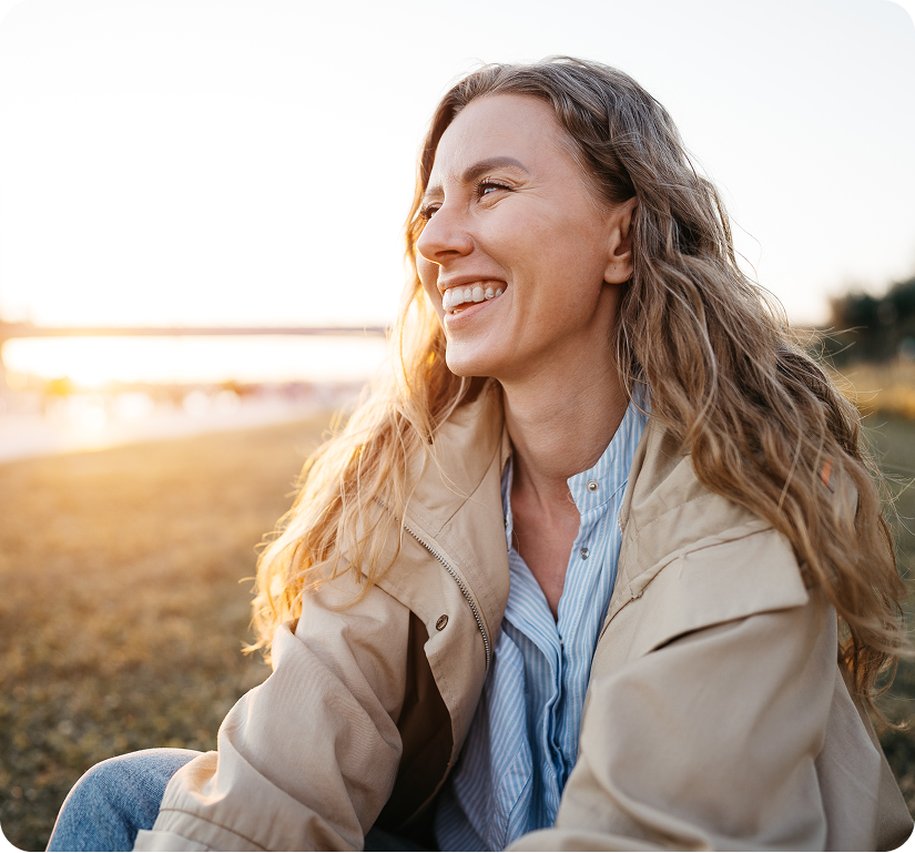 Woman with long wavy hair smiling at sunset in an open field