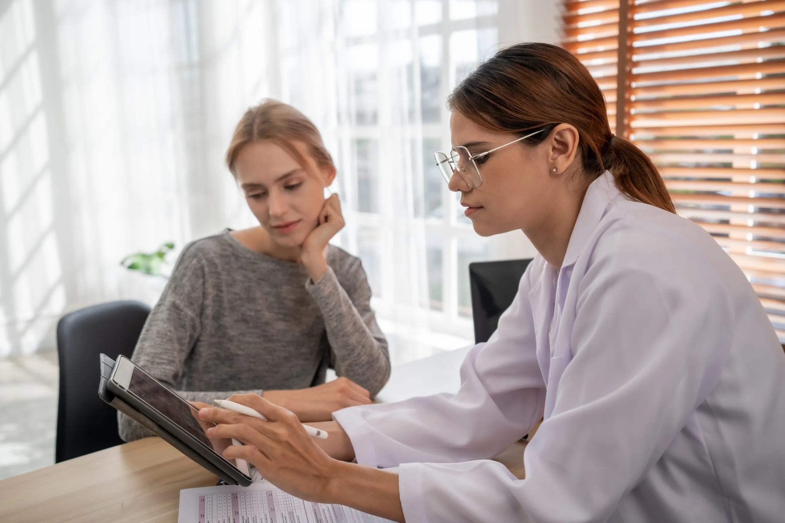 Healthcare provider discussing treatment options with a patient using a tablet in a bright clinical office