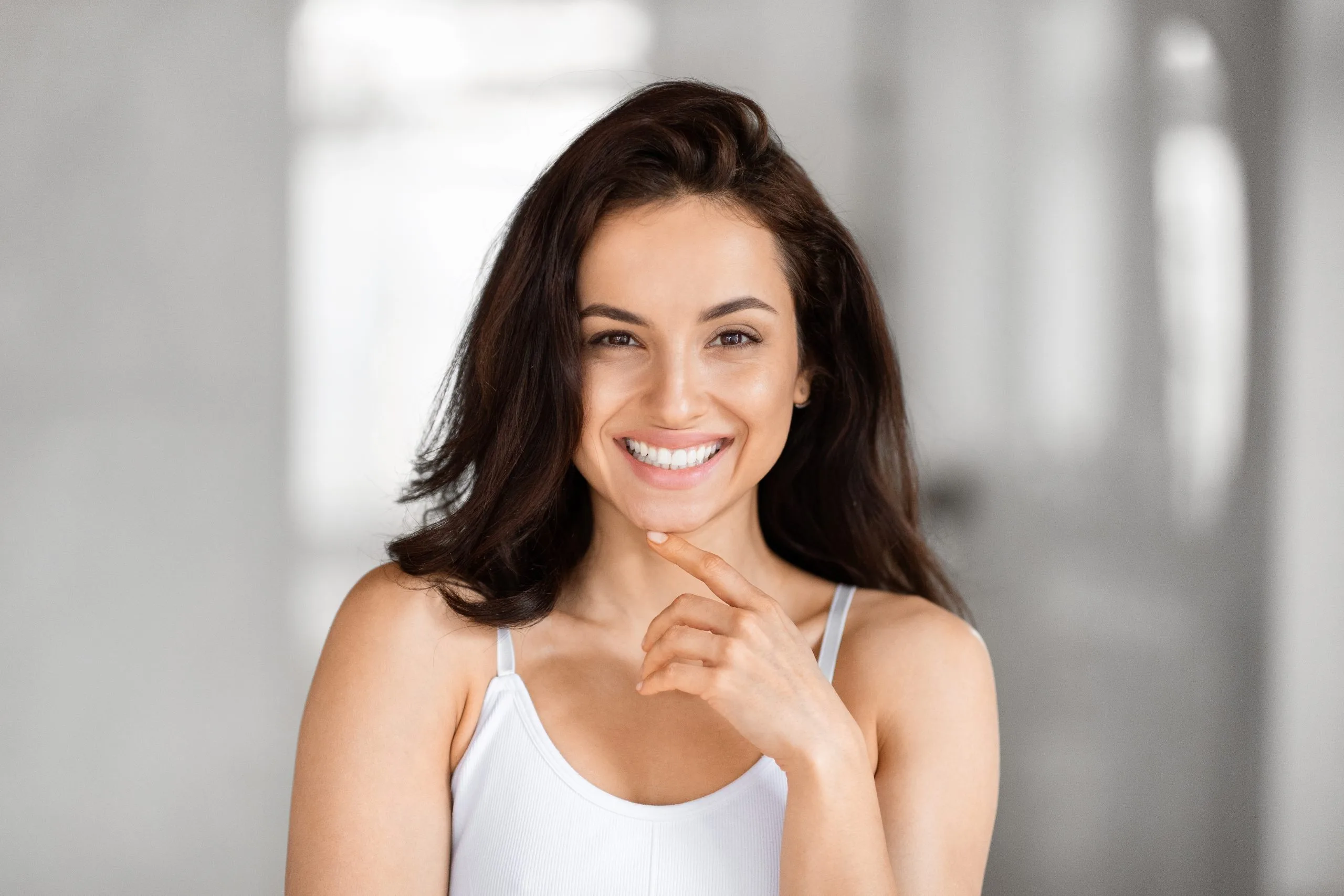 Woman with dark hair smiling and touching her chin in a bright clinical setting