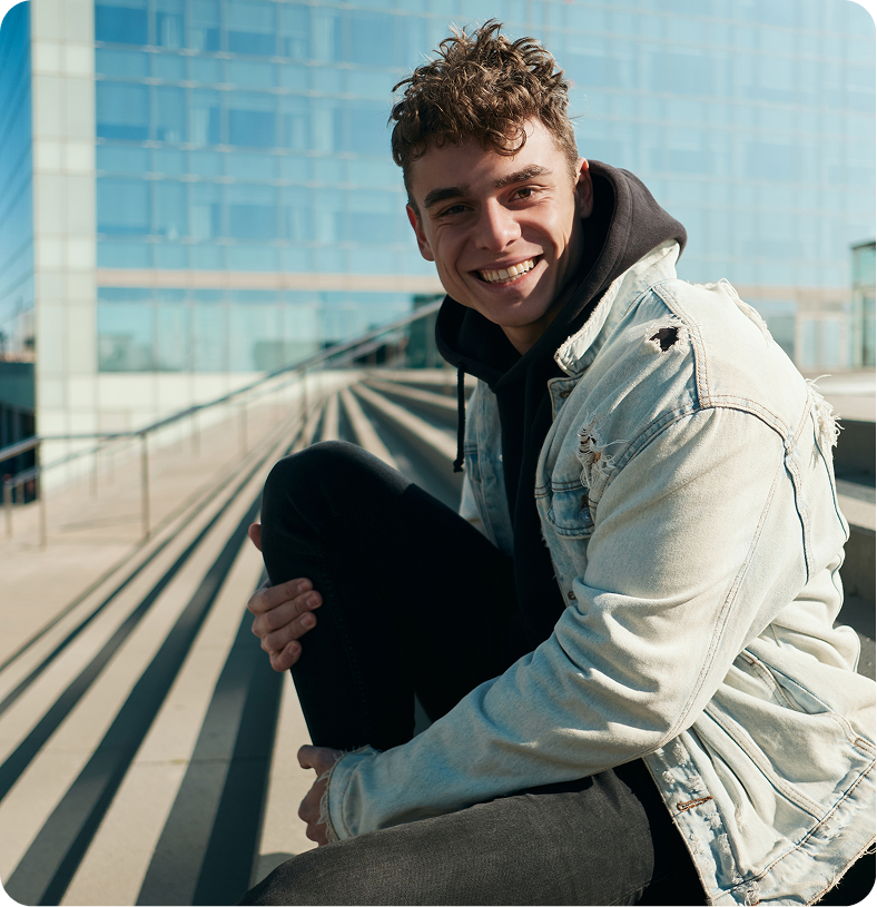 Smiling young man sitting on an urban rooftop overlooking city buildings
