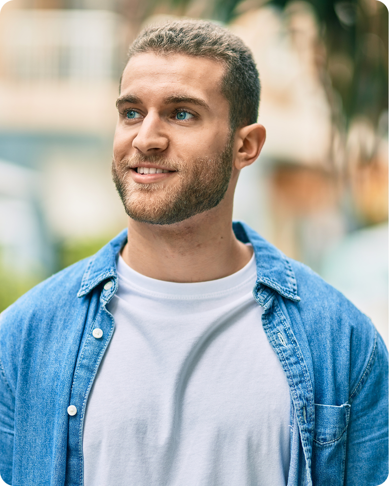 Man with blue eyes smiling outdoors wearing a denim shirt over white t-shirt