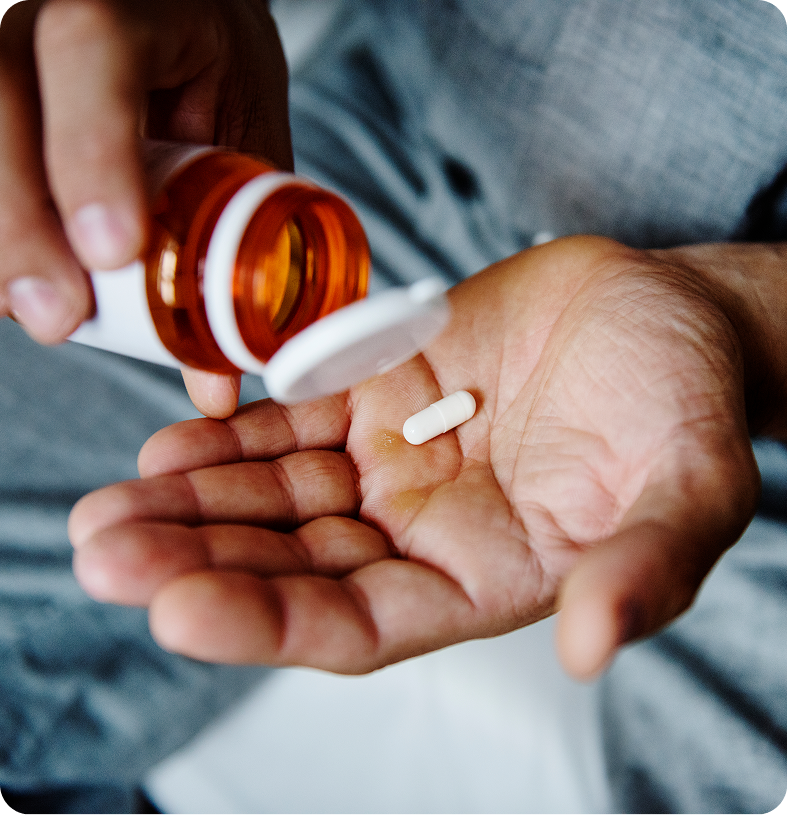 Person pouring white tablet from amber prescription bottle into open palm