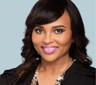 Professional woman in black blazer with pearl necklace smiling against light blue background