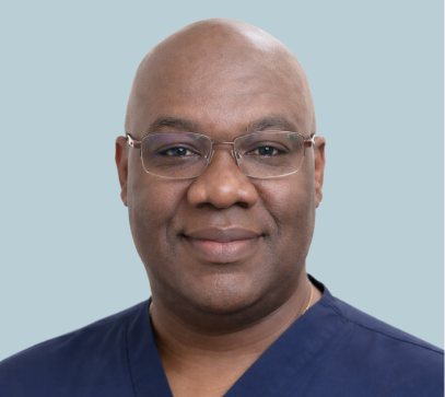 Man wearing glasses and dark blue scrubs smiling at camera against light blue background
