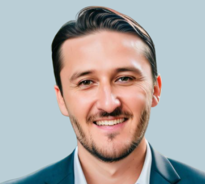 Man with dark hair and facial hair wearing dark blazer smiling at camera against light blue background