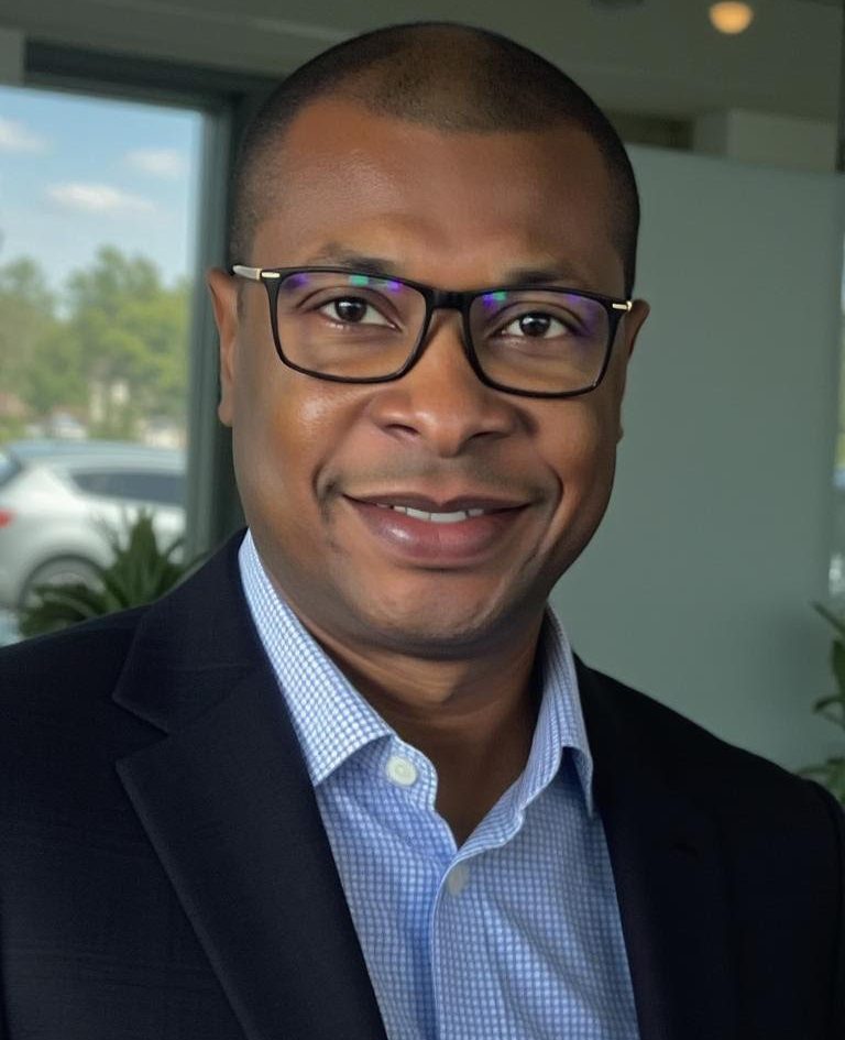 Nixon Jean, man wearing glasses and dark blazer in office setting