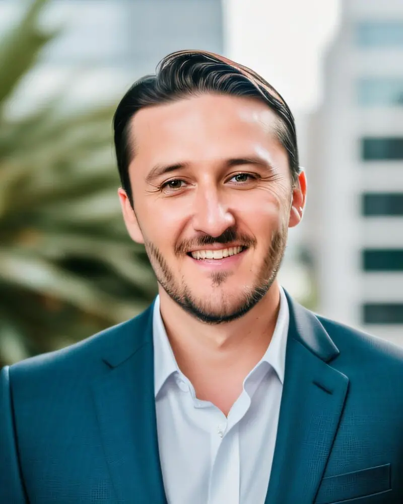 Provider headshot of a man in a teal blazer and white shirt, smiling outdoors with buildings in background