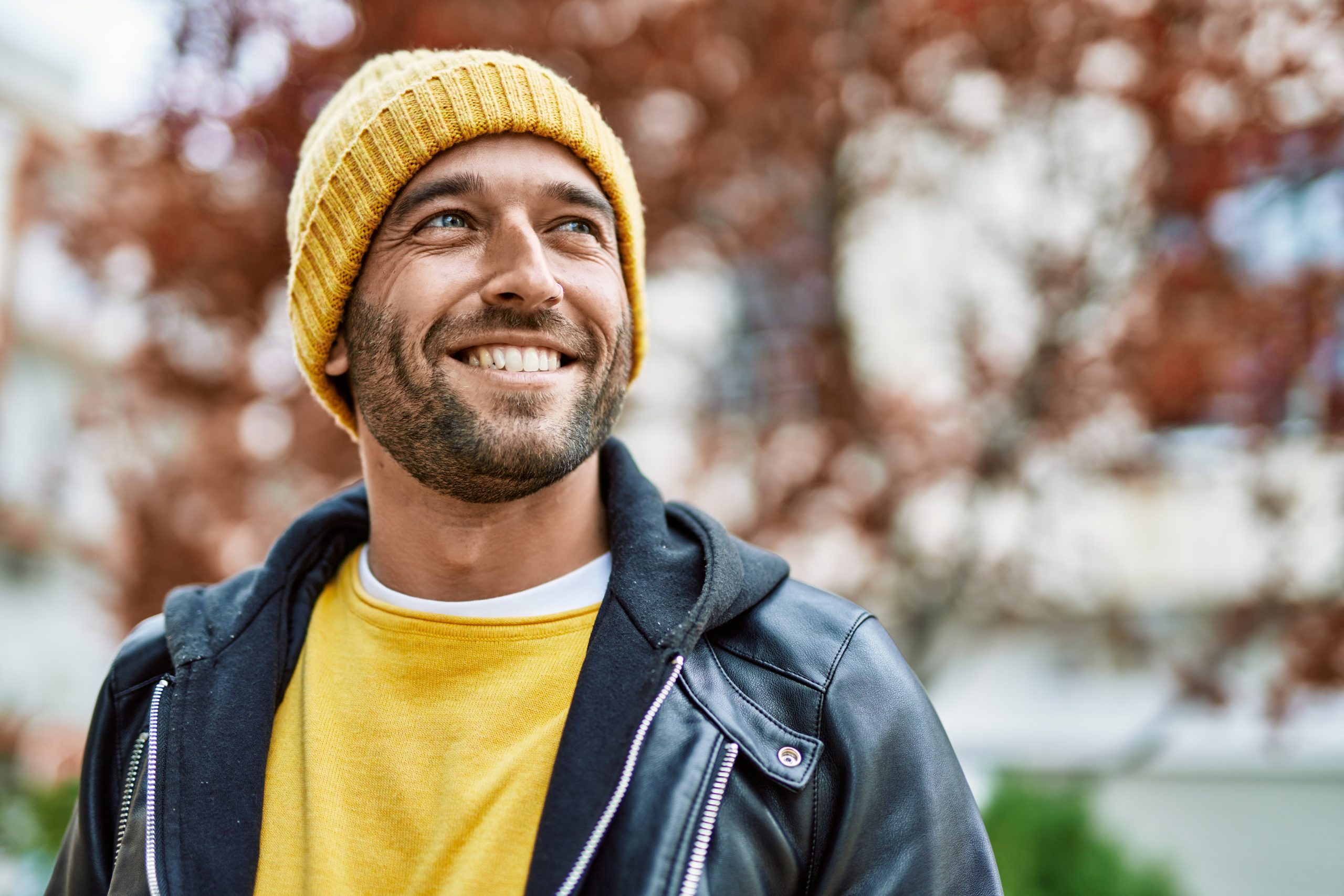 Man wearing yellow beanie and navy jacket smiling outdoors
